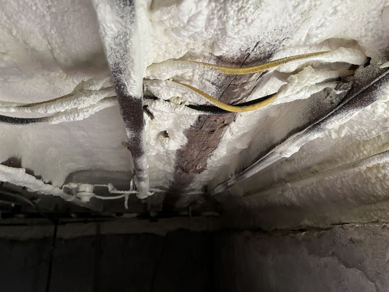 Basement ceiling joists sealed with spray foam around pipes.