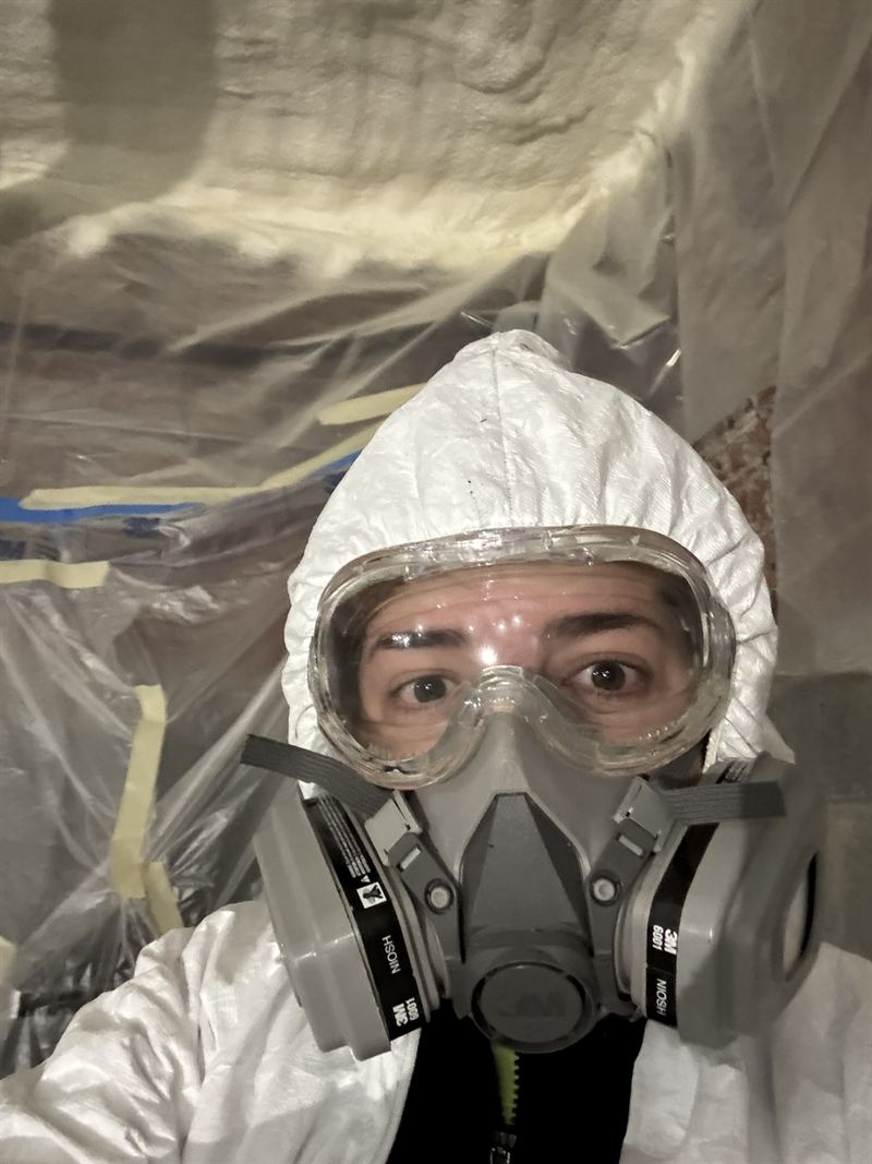 Installer wearing a full-face respirator and protective suit before starting a spray foam application.