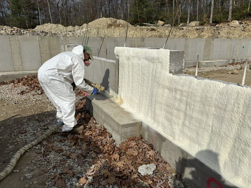 Foundation wall being sprayed with closed-cell foam before backfill.