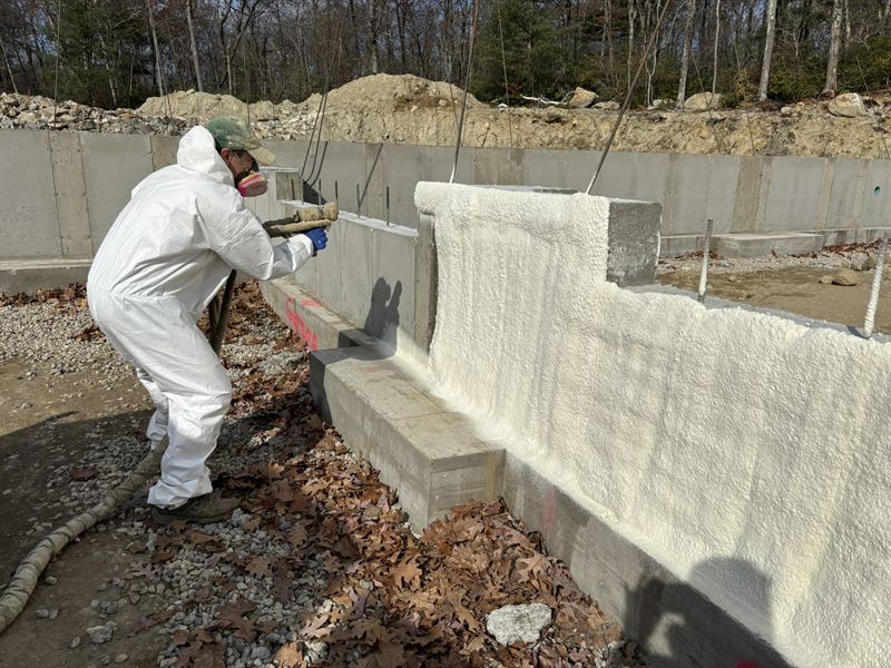 Installer in full protective gear spraying closed-cell foam onto a new foundation wall.