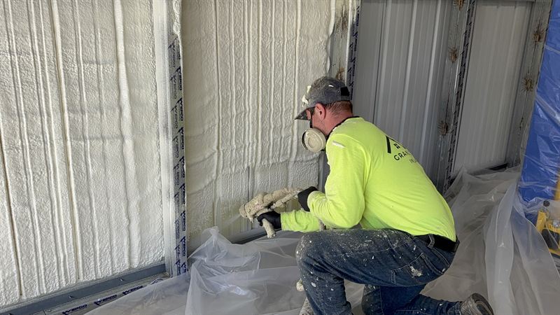 Installer spraying foam around an overhead garage door opening protected with masking.