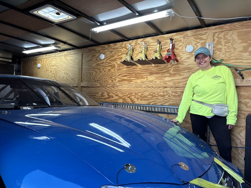 A race car parked inside a finished insulated garage with plywood-lined walls.