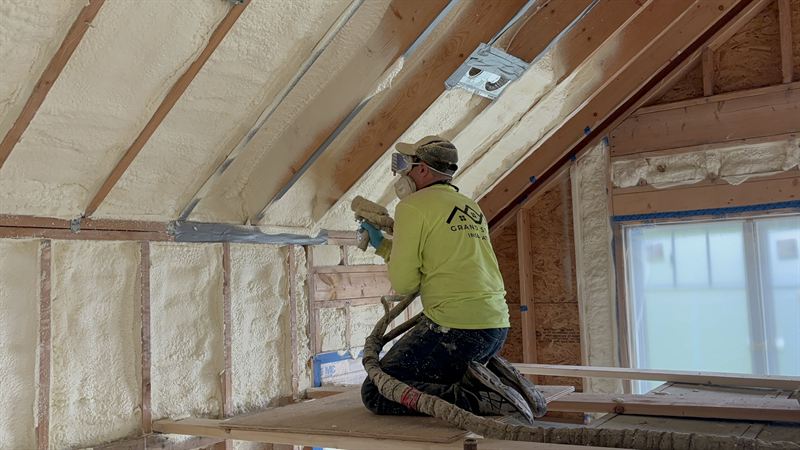 Installer spraying foam between attic rafters from a work platform.