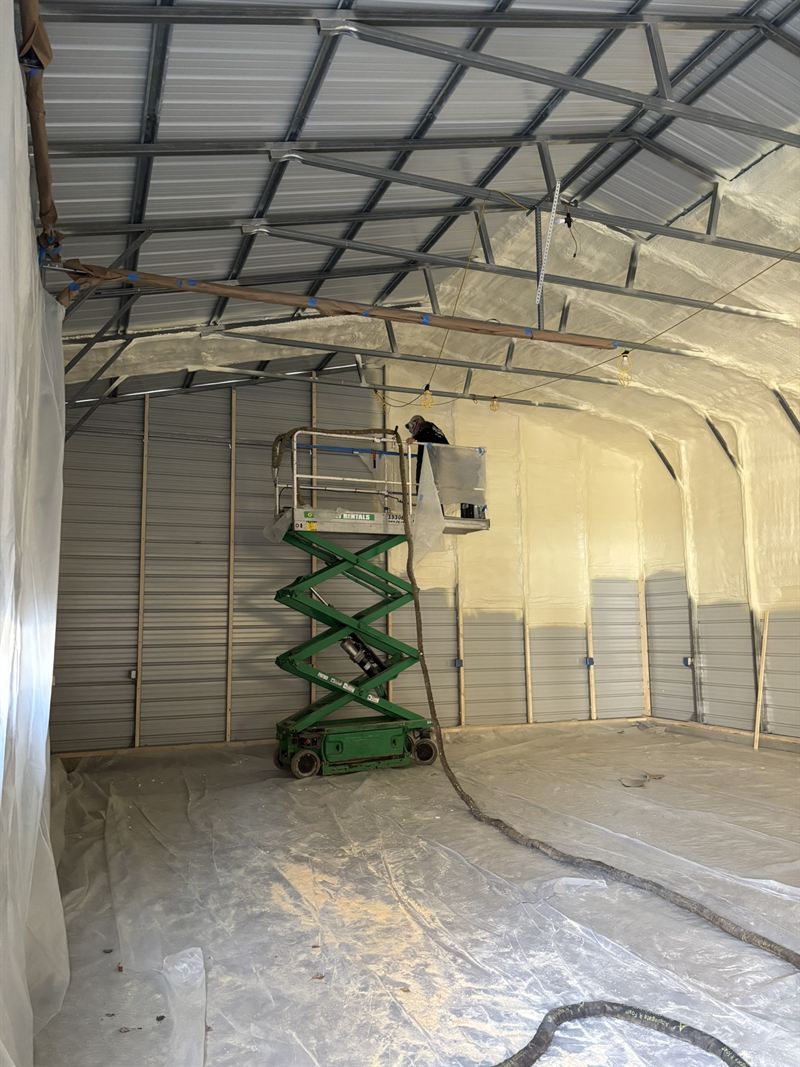 Metal building partway through insulation with one wall sprayed and bare steel still exposed on the other.