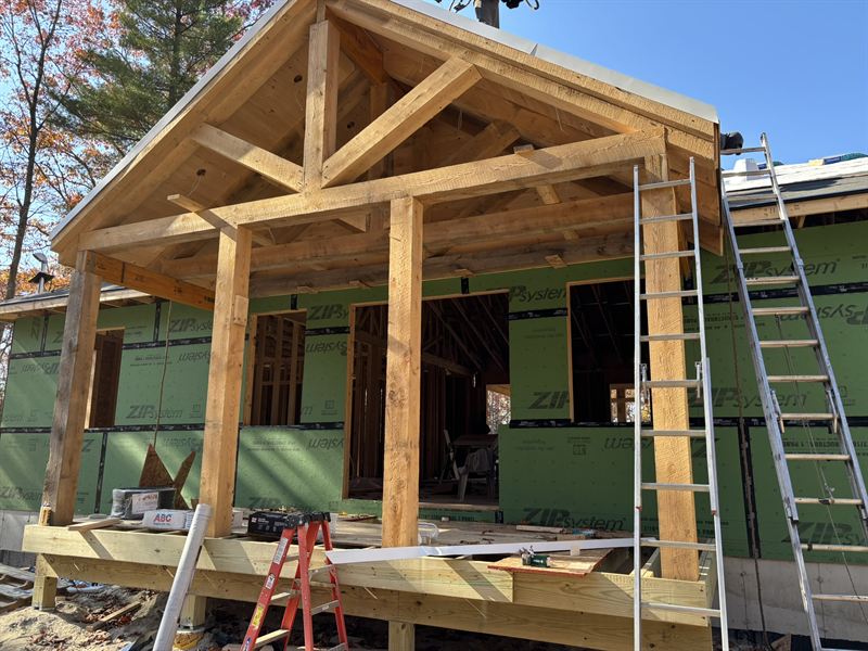 Timber-framed entry porch on a house under construction with sheathing and housewrap in place.